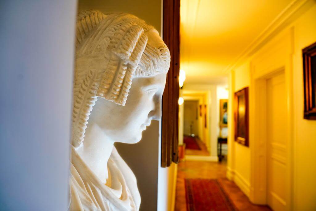 Statua in primo piano presente nel corridoio, che si intravede di sfondo. Foto dai toni caldi